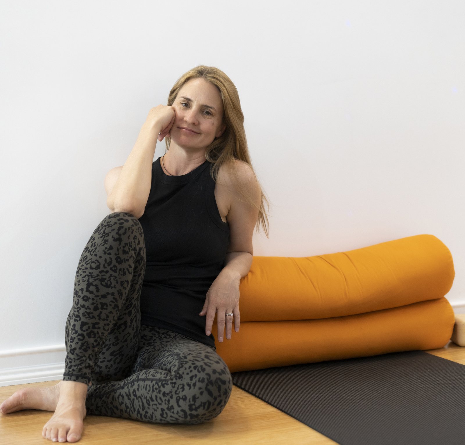 Renae Molden sitting against the studio wall beside two orange bolsters